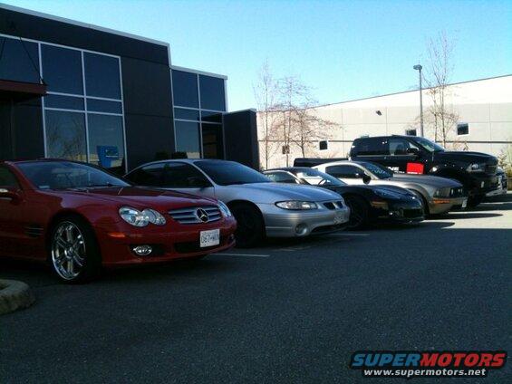Red Mercedes-Benz, silver Pontiac Grand Prix, black Corvette, gray Mustang, and black pickup truck parked in a lot.