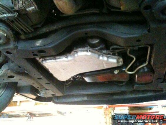 Underside of a vehicle showing transmission pan and fluid lines.