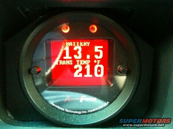 Aeroforce digital gauge showing battery voltage and transmission temperature in a vehicle.
