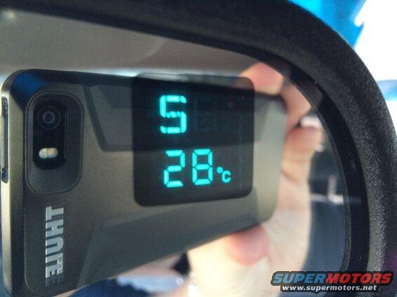 Digital thermometer showing 28°C reflected in a car's rearview mirror.