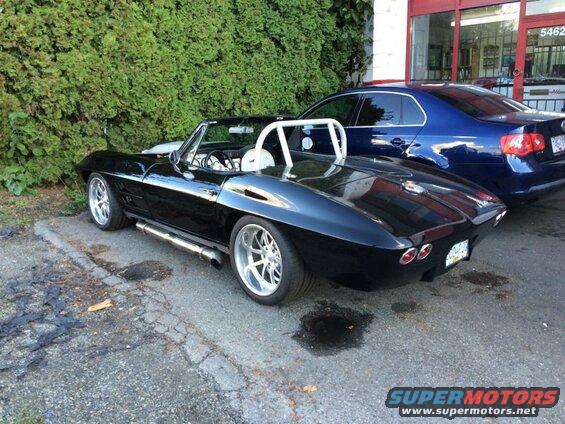 Black convertible sports car with chrome wheels and side exhaust, parked next to a blue sedan.