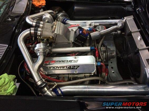 Modified Donovan 427 engine with supercharger and polished aluminum intake piping in a black vehicle.