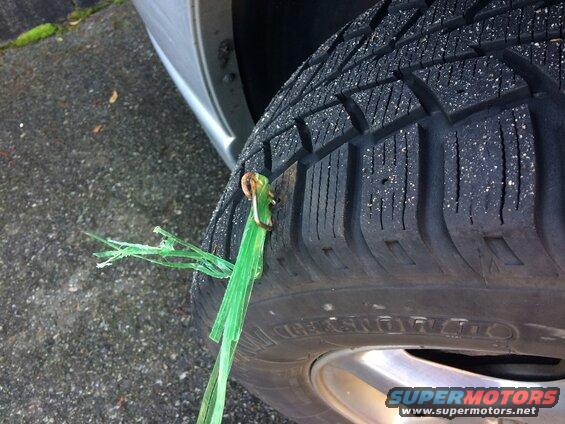 Close-up of a green zip tie used as a tire plug, with tire tread visible.