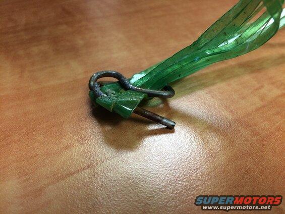 Close-up of a metal loop and pin attached to green plastic on a wooden surface.