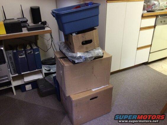 Stack of boxes and a blue bin next to a shelf with binders and electronics.