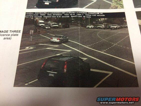 Rear view of a black SUV at an intersection with a red light camera ticket visible.