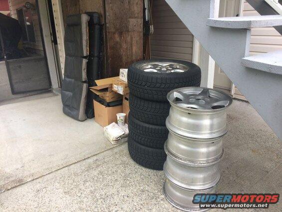 Stack of car tires and alloy wheels next to car seats and boxes.