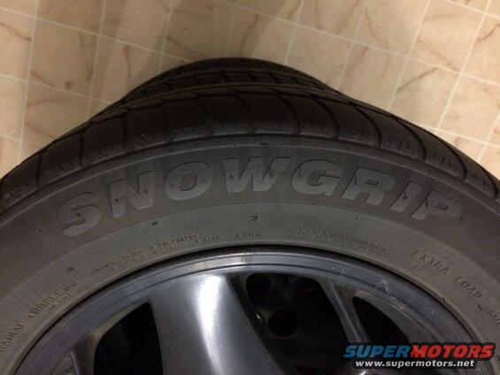 Close-up of a SNOWGRIP tire on a dark gray wheel.