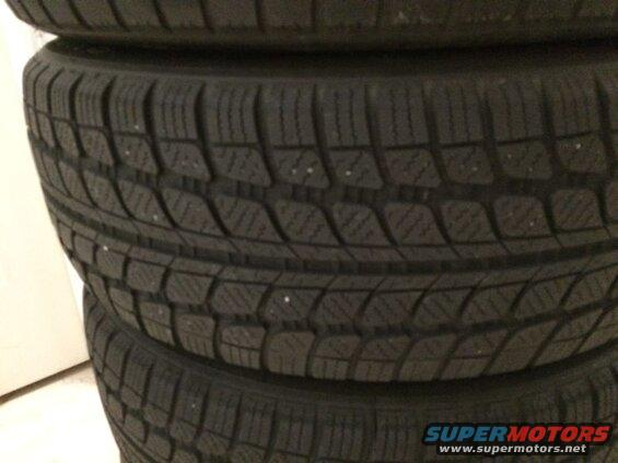Stack of four dark winter tires with visible tread detail and possible studs.