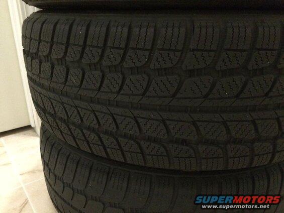 Stack of four black car tires with detailed tread.