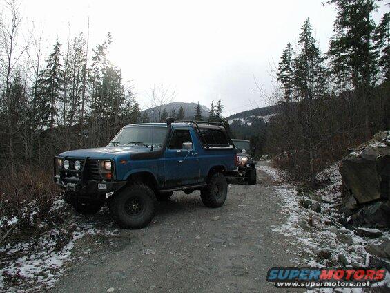 Blue SUV and dark Jeep on a snowy gravel road in a forest.