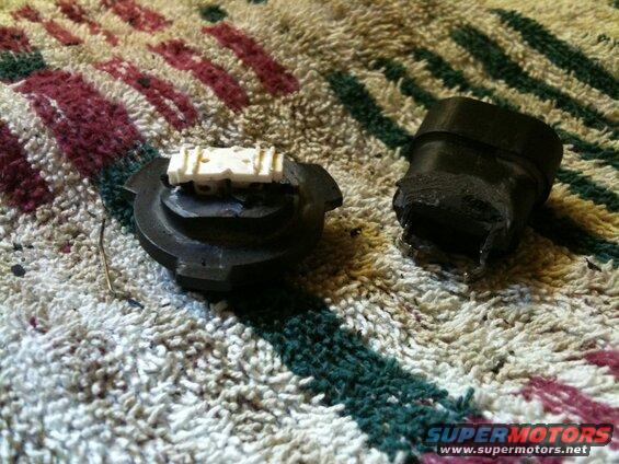 Damaged black plastic automotive parts with a white electrical connector on a rug.