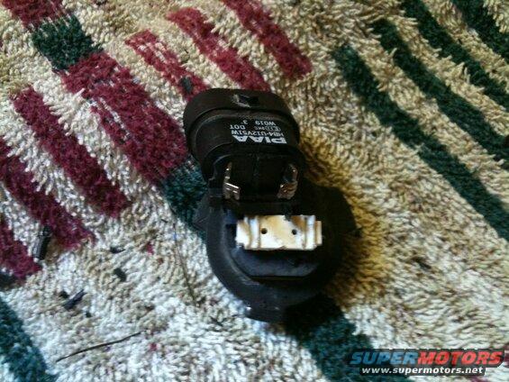 Black PIAA headlight bulb socket with wiring on a rug.