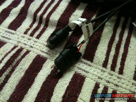 Two black electrical connectors with wiring on a striped towel, one labeled "HIGH BEAM".