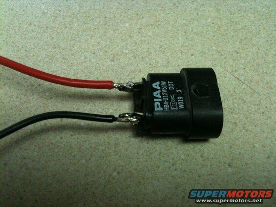Black PIAA headlight bulb connector with red and black wires attached.
