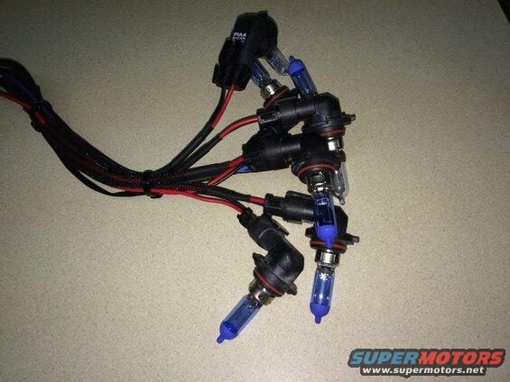 Four PIAA HID bulbs with wiring harnesses on a speckled surface.