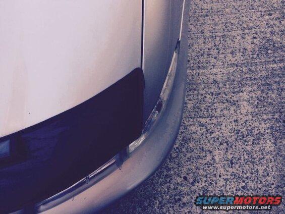 Close-up of silver car front corner with dark trim and concrete.