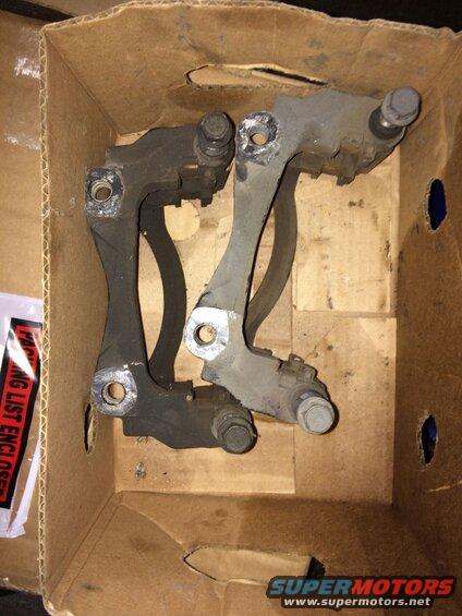 Two used brake caliper brackets in a cardboard box.