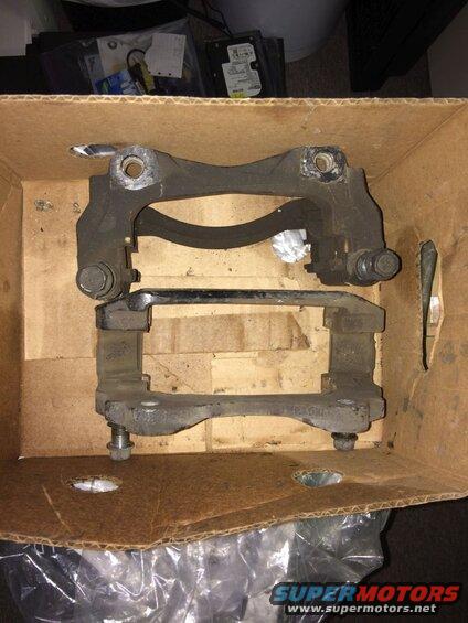 Two black brake caliper brackets in a cardboard box.