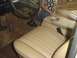 1978 Ford Bronco - The interior of a vehicle features tan vinyl seats and a floor-mounted shifter, with a person's hand resting on the center console.