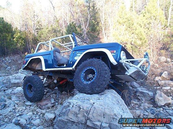 Blue 1977 Ford Bronco with roll cage on rocky terrain