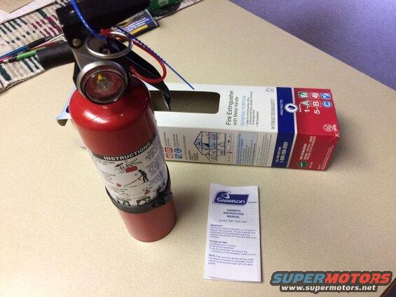 Red fire extinguisher, box, and owner's manual on a table.