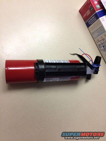 Red fire extinguisher with black nozzle and blue/red tie seal next to a box.
