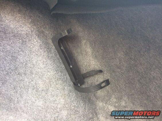 Black plastic bracket with strap mounted on gray carpet in car trunk