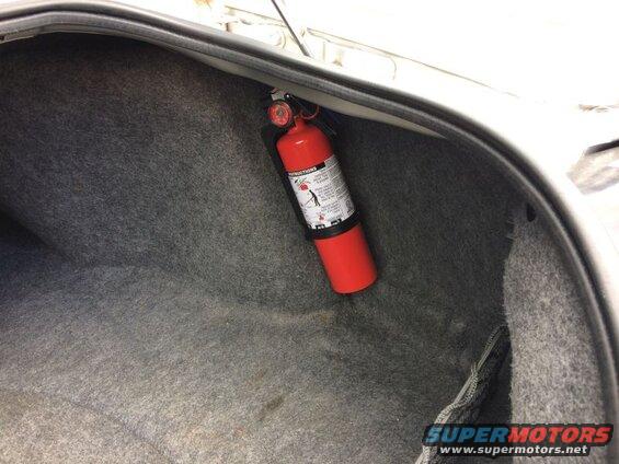 Red fire extinguisher mounted in the trunk of a car.