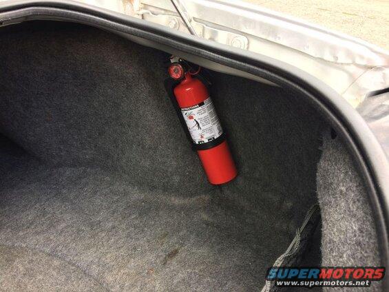 Red fire extinguisher mounted in the trunk of a car.
