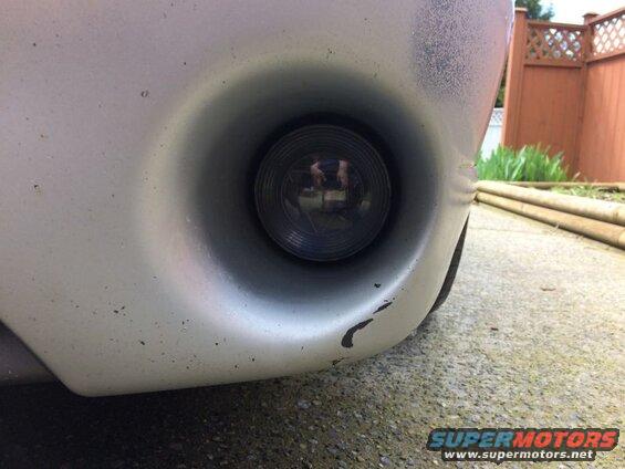 Driver's side fog light assembly on a silver car bumper, low angle view.