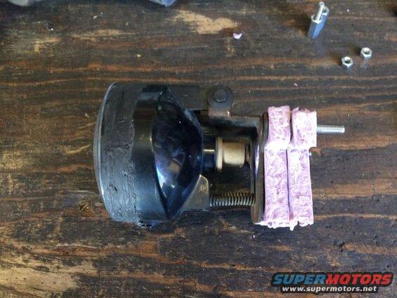 Modified headlight assembly with pink foam padding and bolt on wooden surface.