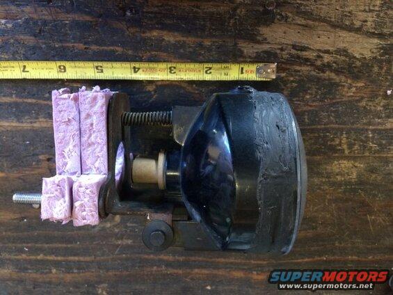 Black headlight assembly clamped in a vise with a measuring tape.