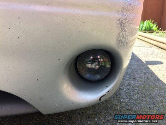 Silver car bumper with fog light and paint chips.