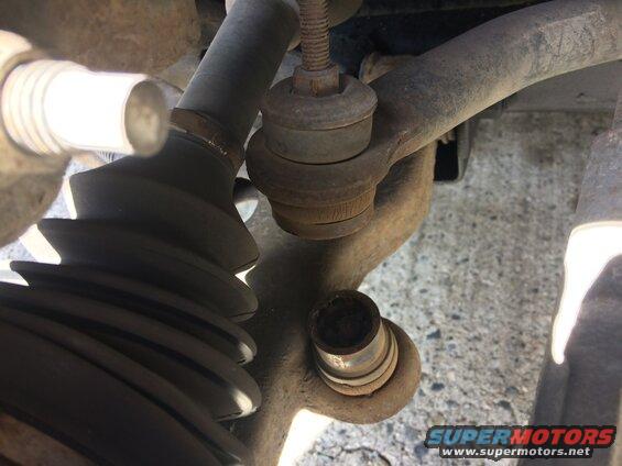 Close-up of rusted car suspension part with torn rubber boot.