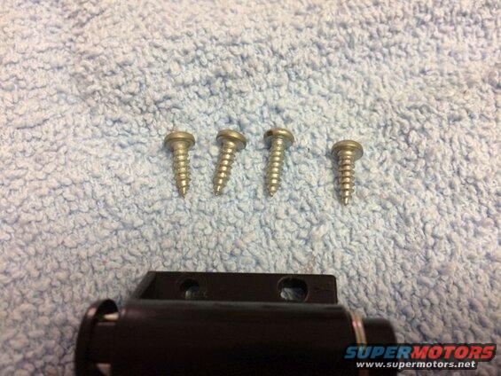 Four screws on a textured surface with a black car part.