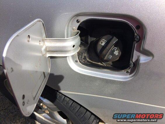 Open fuel filler door on a silver car, showing the fuel cap with symbols.