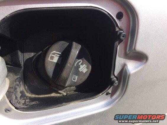 Close-up of a silver vehicle's fuel filler door and cap with symbols.