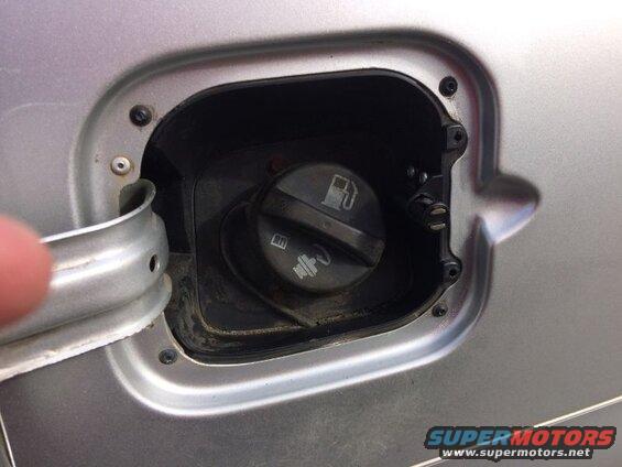 Open fuel filler door on a silver car, showing gas cap and detached door.