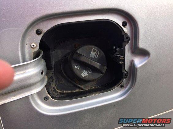 Silver vehicle fuel filler door open, showing gas cap and mechanism.