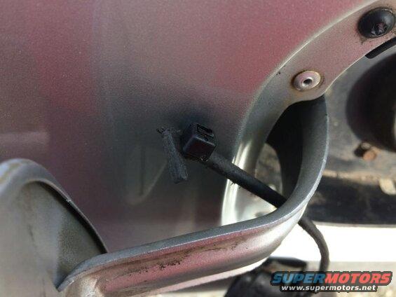 Close-up of a black plastic clip holding a wire on a car's body panel near the fuel filler.