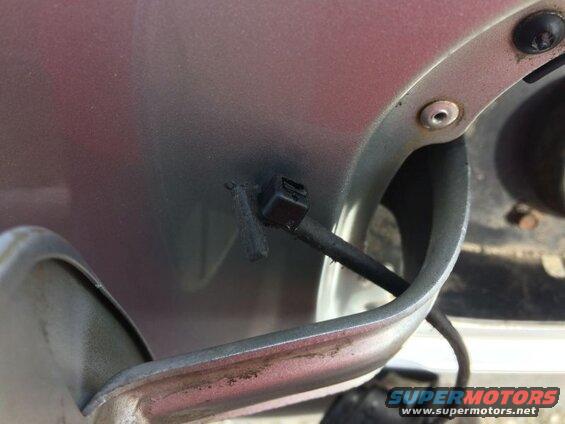 Close-up of black plastic clip on cable near fuel filler door on vehicle.