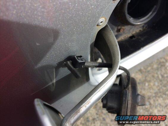 Close-up of a car's fuel filler neck and cap, with a black clip holding a wire.