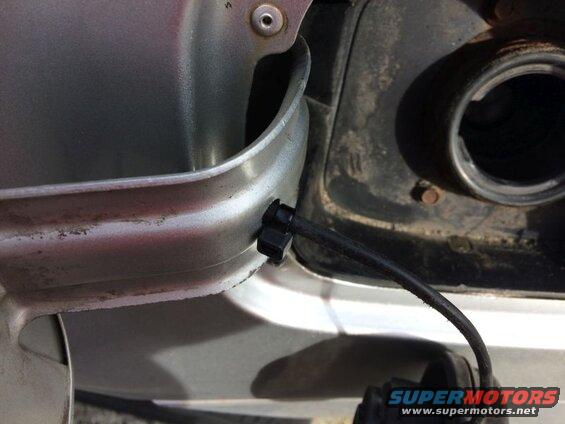 Black fuel filler neck hose attached to silver vehicle's fuel door opening with a clip.