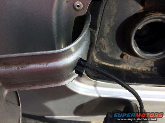 Close-up of a black cable attached to a clip on a silver car's fuel filler door, leading to the open fuel neck.