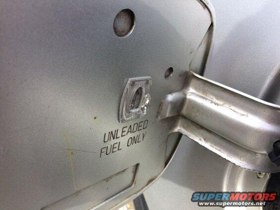 Close-up of a silver car's fuel door with "UNLEADED FUEL ONLY" text and a clear plastic cap.