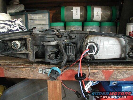 Headlight assembly with wires and bulb socket connected, on a workbench.