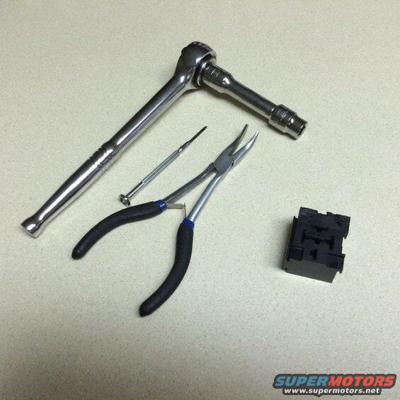 Tools including a ratchet, pliers, screwdriver, and a black electrical component.