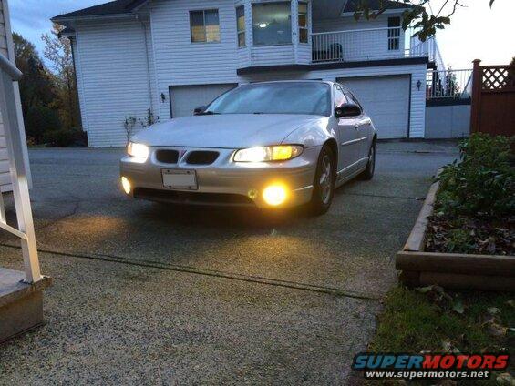 Silver 2002 Pontiac Grand Prix sedan with headlights and fog lights on, parked in front of a house.