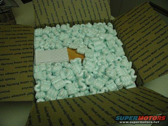 Open box with packing peanuts and a small white and checkered box.